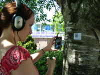 Scanning a QR code outside the Playhouse to hear audio under a shady tree at the Living Voices Showcase